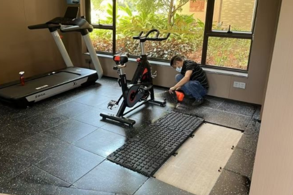 Installing thick gym rubber floor tiles in a heavy weightlifting area with tools and adhesive shown