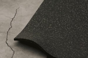Uneven concrete subfloor with cracks under partially installed speckled rubber tile.
