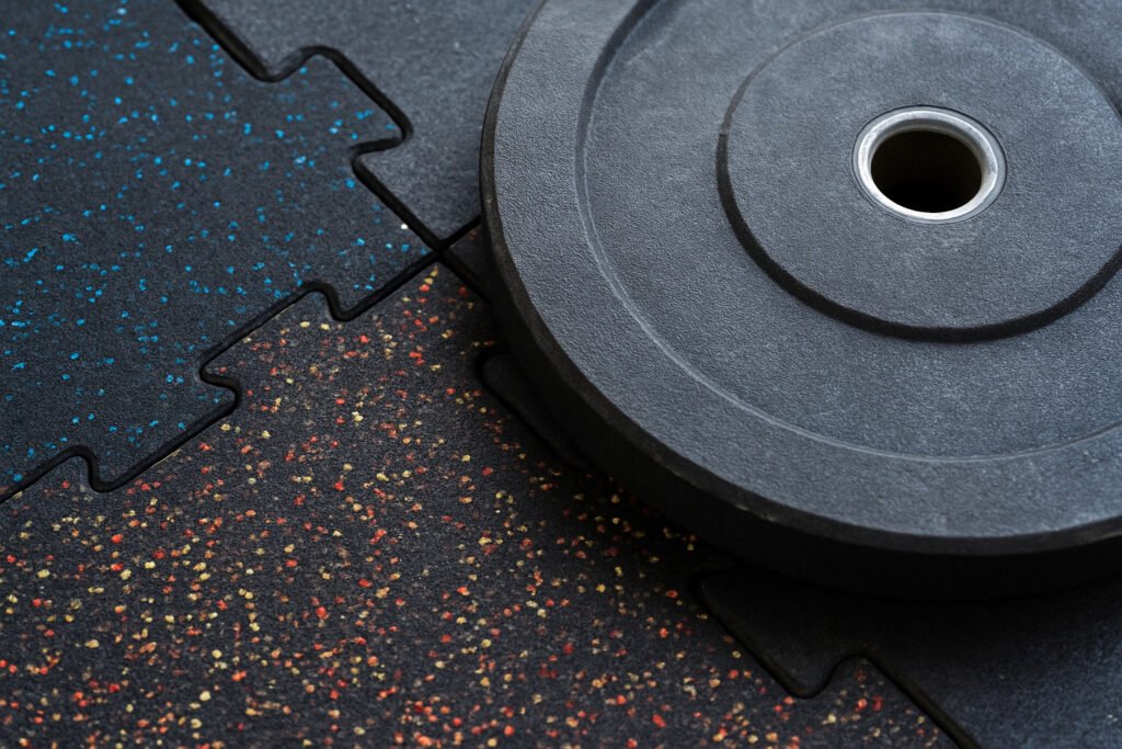 Close-up of interlocking rubber gym tiles under a weight plate for noise and impact reduction