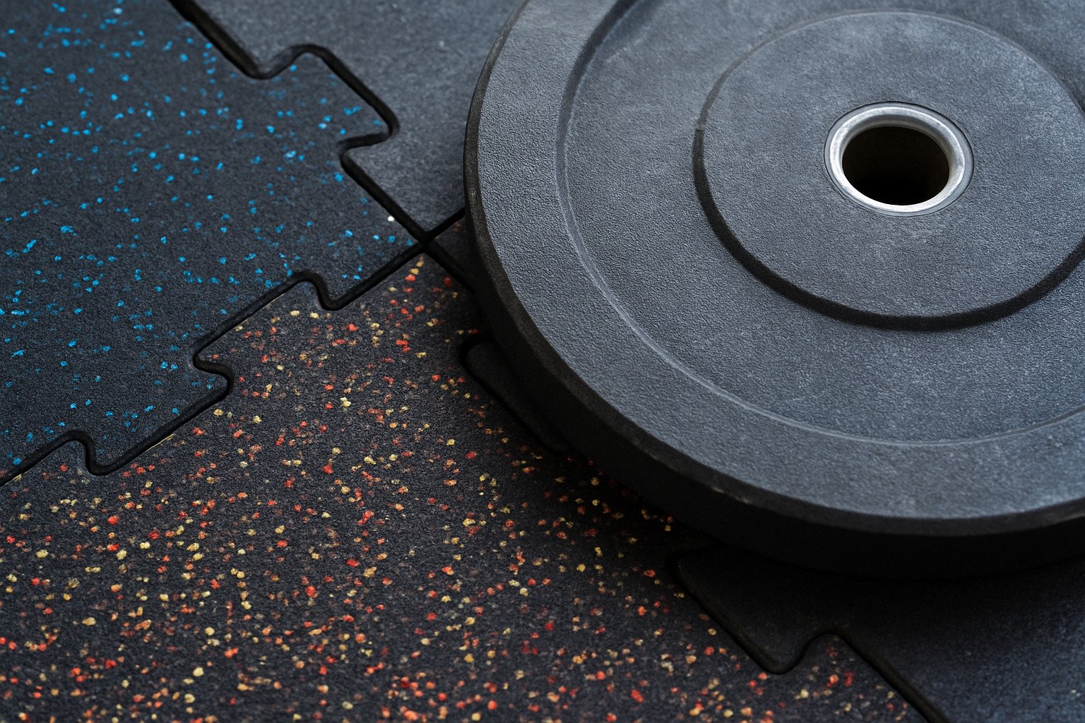 Close-up of interlocking rubber gym tiles under a weight plate for noise and impact reduction