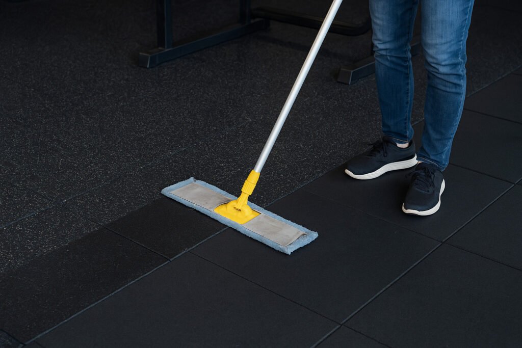 Person cleaning rubber flooring in a commercial gym with a mop and bucket