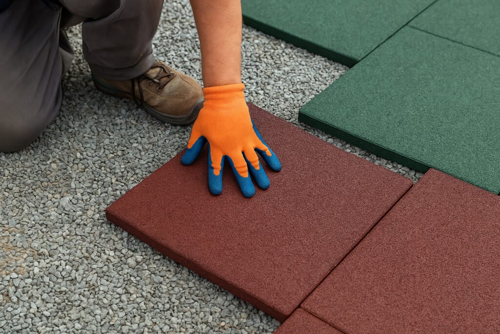 Worker installing red and green interlocking rubber tiles on outdoor gravel base