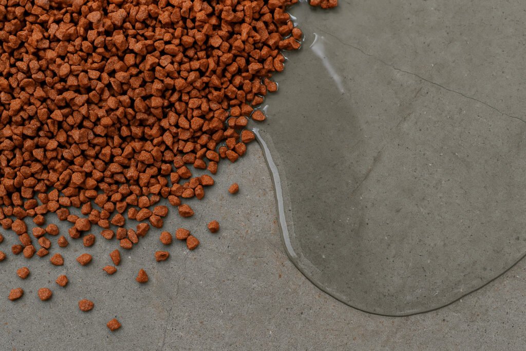 Close-up photo of EPDM granules next to liquid PU binder on a concrete surface, showing materials used in EPDM wet pour flooring installation.
