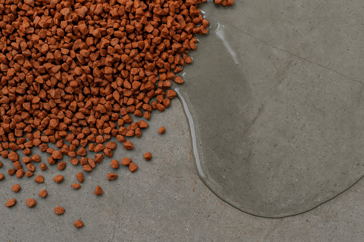 Close-up photo of EPDM granules next to liquid PU binder on a concrete surface, showing materials used in EPDM wet pour flooring installation.