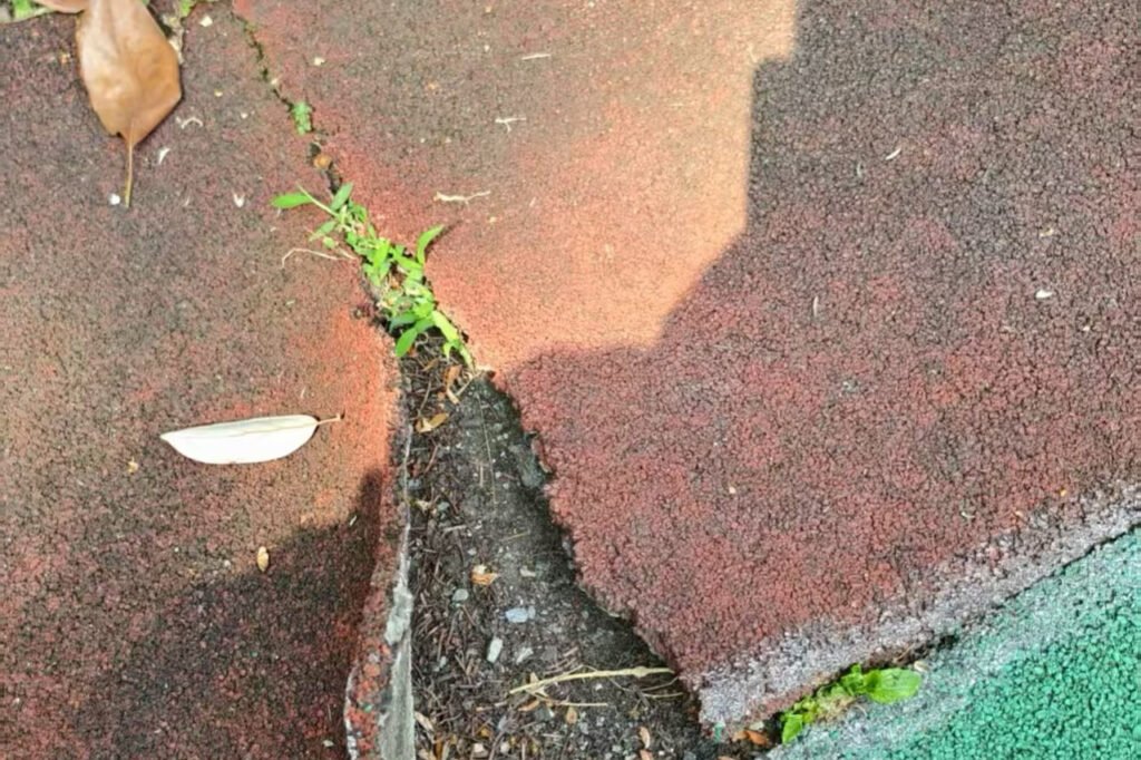 Close-up view of a colorful EPDM wet pour playground surface with a visible crack running through it, showing how the rubber flooring has split over time.