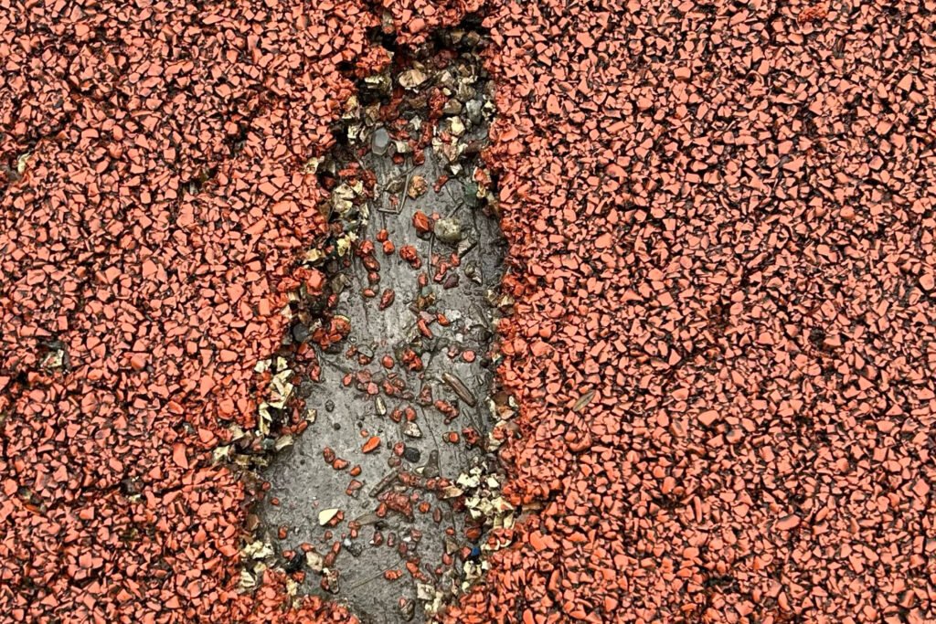 Close-up view of an EPDM wet pour playground surface with a visible raised bubble or bulge, showing moisture or air trapped under the rubber flooring.