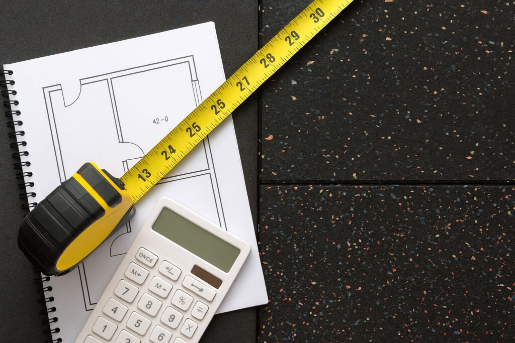 A flat lay photo showing a tape measure, calculator, and rubber roll floor plan, used for estimating gym flooring quantity.